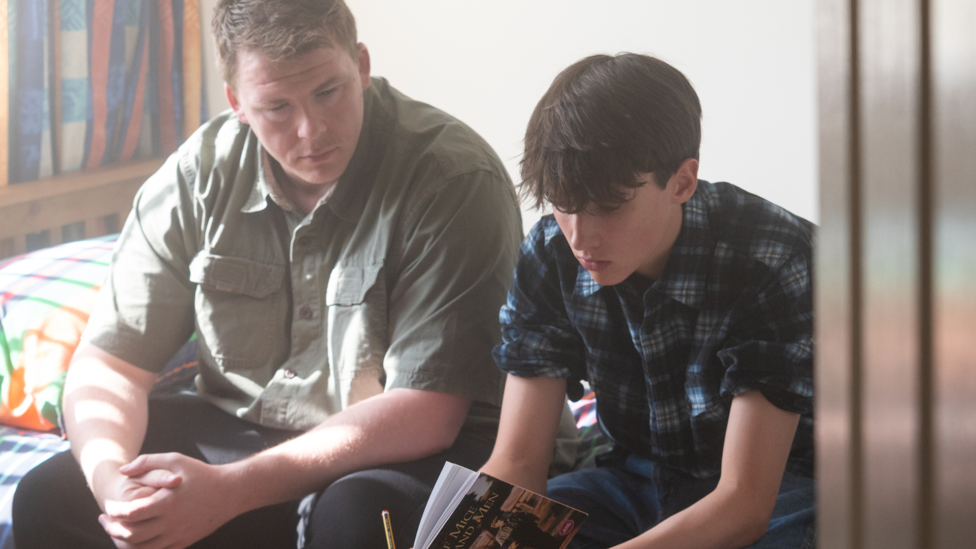 A foster father sits with his foster son to help him read 'Of Mice and Men' for school.